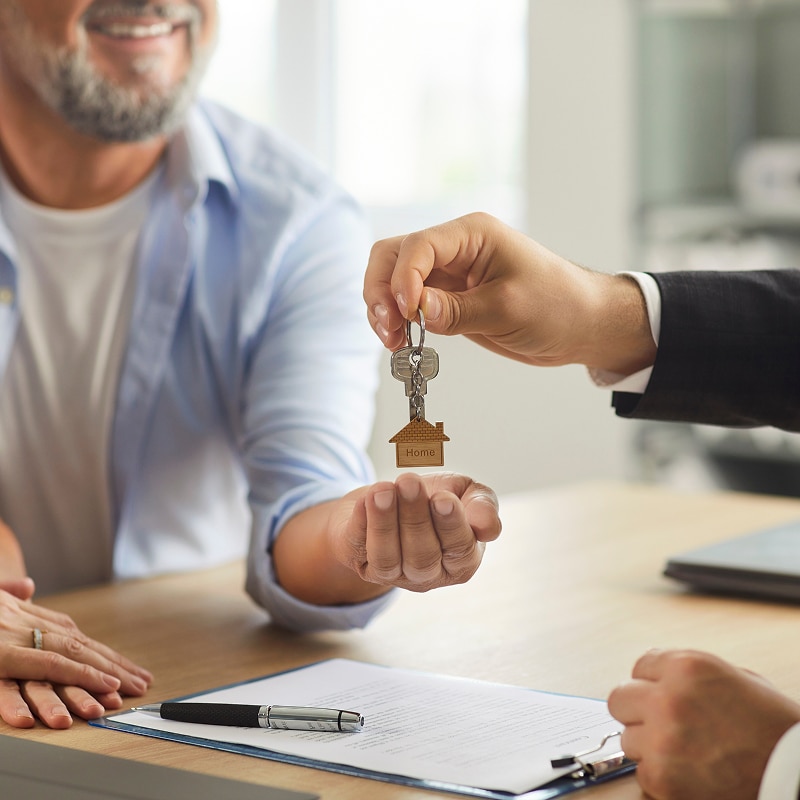 Remise des clés "Home" d'une maison par un agent à un acheteur souriant. Contrat et couple à la table de clôture immobilière.
